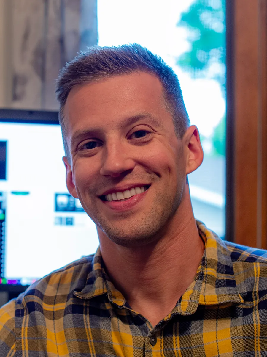 Dr. Thomas Adolphs - A man with short brown hair and a yellow plaid shirt smiles at the camera indoors, with a window and a computer monitor in the background.