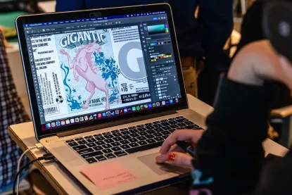 Person using Adobe Illustrator on a MacBook, designing a retro-style cover titled "Gigantic" featuring a pink mythological creature.