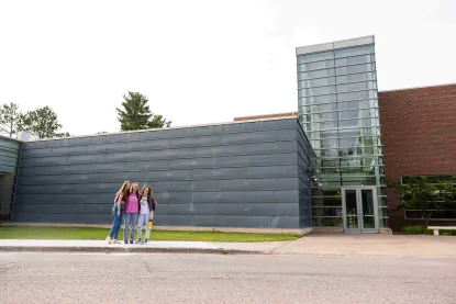 Three students standing in front of the art and design building on NMU's campus