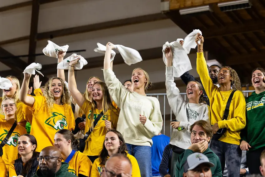 A group of NMU Alumni waving white towels at a NMU hockey game in the Berry Events Center.